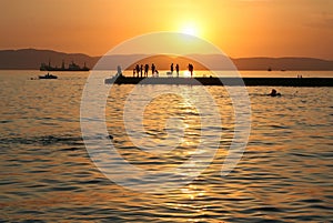 Golden sunset at the sea. Pier, silhouettes of people, sun sets, mountains, calm sea, boats