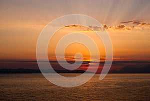 Golden sunset with sun covered by clouds, rays above clouds