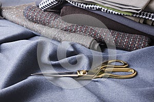 Golden tailor`s scissors on the blue woolen fabric, stack of suiting fabrics