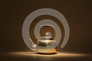 golden teapot on a brown background and overhead lighting that charges it with mystery