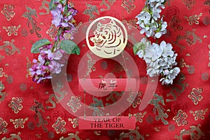 Golden tiger sign and branches of white and pink sakura cherry blossom on red fabric with chinese ornament birds and dragons.