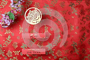 Golden tiger symbol and branch of pink sakura cherry blossom on red fabric with traditional chinese ornament birds and dragons.