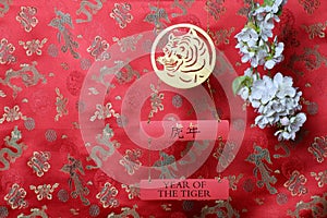 Golden tiger symbol and branch of white sakura cherry blossom on red fabric with traditional chinese ornament birds and dragons.