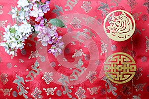 Golden tiger symbol and branches of white and pink sakura cherry blossom on red fabric with traditional chinese ornament birds and