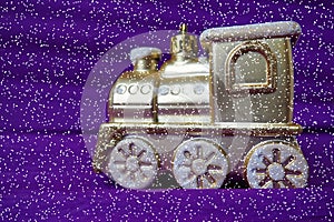 Golden toy train locomotive on a purple and lilac gradient background. New Year or Christmas card. Icicles and snow on