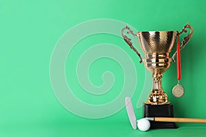 Golden trophy cup, medal, golf club and ball on color background