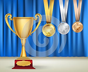 Golden trophy cup and set of medals with ribbons on blue curtain