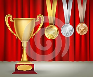 Golden trophy cup and set of medals with ribbons on red curtain