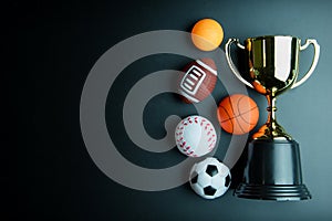 Golden trophy, Football toy, Baseball toy, Ping pong ball, Basketball toy and Rugby toy isolated on black background with copy sp