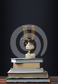 Golden trophy on pile of books, against blackboard, learning/achievement concept
