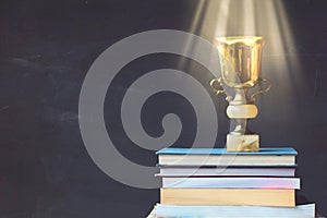 Golden trophy on pile of books, against blackboard, with sun ray