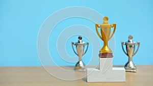 Golden trophy standing on white podium with two silver trophy at back