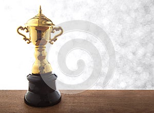 Golden trophy on wooden table over abstact white bokeh background. Winning awards with copy space.