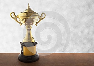 Golden trophy on wooden table over abstact white bokeh background. Winning awards with copy space.