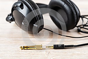 Golden TRS adapter and jack near black wired over ear headphones on a desk. Gold plated plugs for high quality audio. Modern