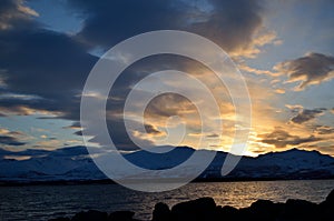 Golden vibrant sunset over snowy mountain and fjord