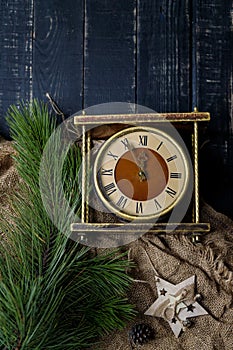 Golden vintage clock, pine branches, sackcloth and wooden toy star on black background. Merry Christmas, New Year eve