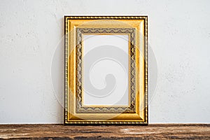 Golden vintage photo frame on old wooden table over white wall b