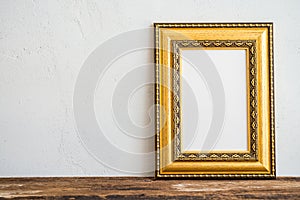 Golden vintage photo frame on old wooden table over white wall b