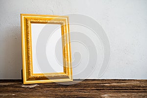 Golden vintage photo frame on old wooden table over white wall b