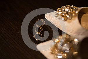 Golden wedding ring near the beige shoes with shiny stones on them. Wedding