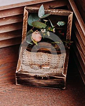 Golden wedding rings in the beautiful rustic box with flowers inside and on the wooden background