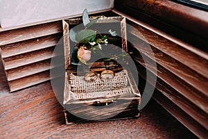 Golden wedding rings in the beautiful rustic box with flowers inside and on the wooden background