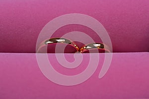 Golden wedding rings on pink background, close up