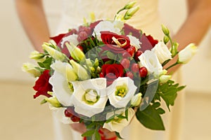 Golden wedding rings among red berries and white and red roses and green buds of wedding bouquet