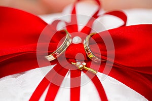 Golden wedding rings on red and white ring pillow