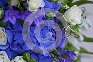 Golden wedding rings with on wedding bouquet of white and blue flowers