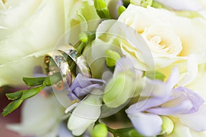 Golden wedding rings on wedding bouquet of white roses and violet flowers