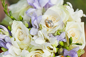 Golden wedding rings on wedding bouquet of white and violet flowers