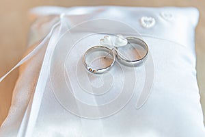 Golden wedding rings on white pillow ready for ceremony. The newlyweds will exchange their rings and say their promise