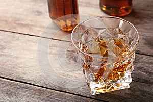 Golden whiskey in glass with ice cubes on table.