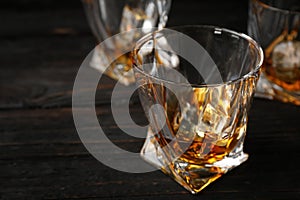 Golden whiskey in glass with ice cubes on wooden table.