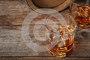 Golden whiskey in glass with ice cubes on wooden table