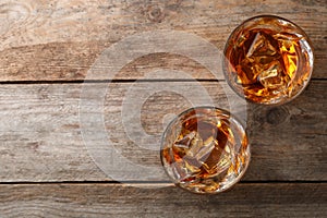 Golden whiskey in glasses with ice cubes on wooden table