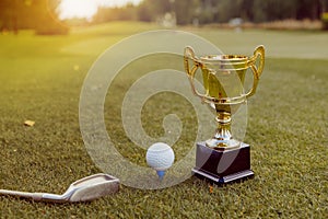 Golden winner cup with golf ball and golf club on green grass on golf course
