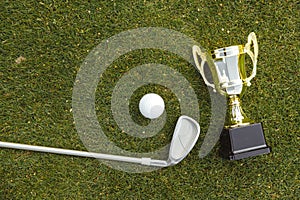 Golden winner cup with golf ball and golf club on green grass on golf course