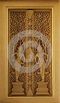 The golden wooden temple door is carved with two deities and exquisite ancient Thai patterns. Decorations at the entrance to the