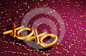 Golden xoxo foil balloon on pink background with gold glitter confetti. Top view. Valentine`s day background. Celebration party