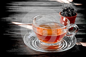 golden yellow amber tea in a clear colored teacup is placed on a dark wooden table and hard shadows background