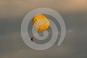 A golden yellow parasailing flying through a beautiful dramatic evening sky