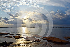 Golden Yellow Sun with Bright Sunlight rising from behind Clouds with Reflection in Sea Water - Morning Sky at Beach