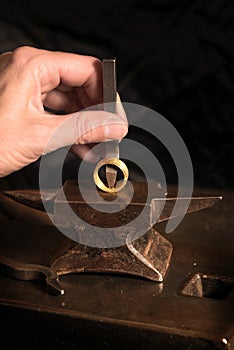 Goldsmith hand punches a hallmark into a golden ring on a small photo