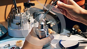 A goldsmith in jewelry working with ring. Working jeweller puts yellow gemstone on a ring.