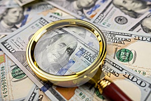 Golen magnifying glass on different dollars money as financial background