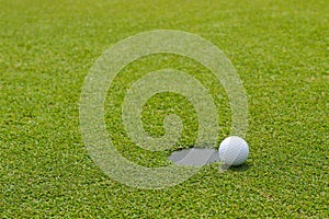 Golf ball at the edge of putting cup hold at putting green