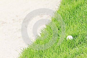 Golf ball on green grass near sand bunker